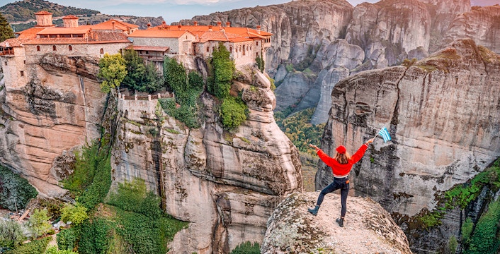 Tourist with Greek flag admiring Meteora rock formations and monastery, Greece.