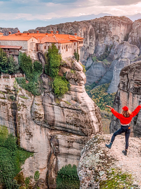 Tourist with Greek flag admiring Meteora rock formations and monastery, Greece.