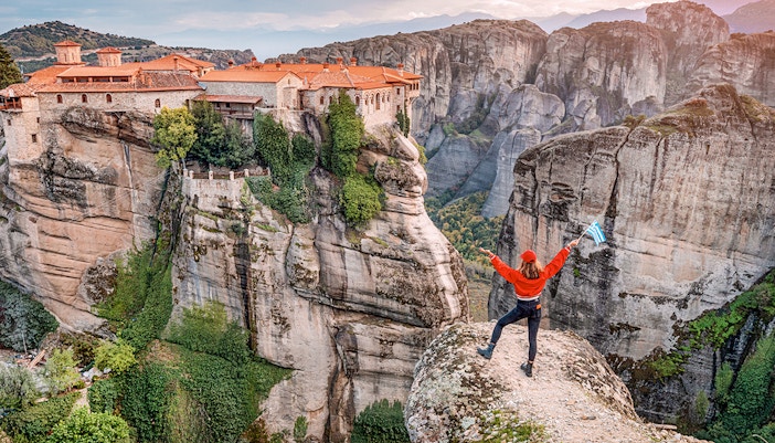 Tourist with Greek flag admiring Meteora rock formations and monastery, Greece.