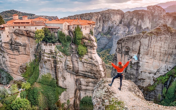 Tourist with Greek flag admiring Meteora rock formations and monastery, Greece.