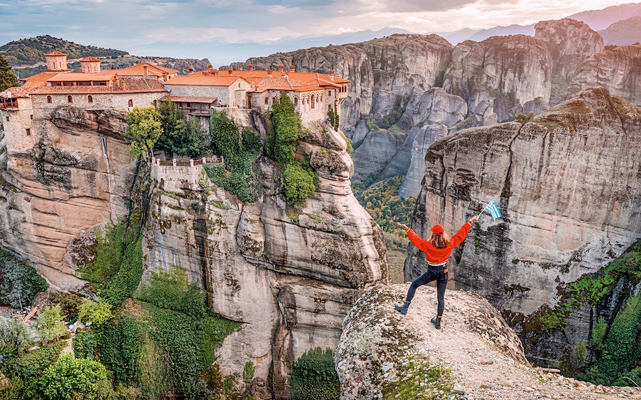 Tourist with Greek flag admiring Meteora rock formations and monastery, Greece.