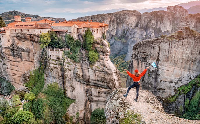 Tourist with Greek flag admiring Meteora rock formations and monastery, Greece.