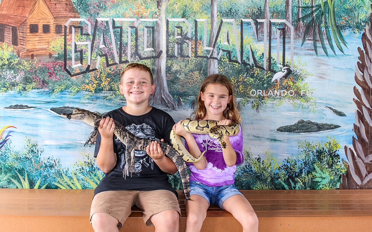 Children holding reptiles at Gatorland, Orlando backdrop.