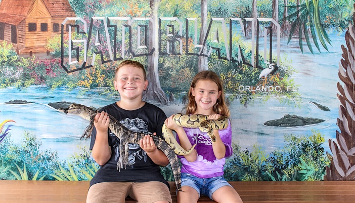 Children holding reptiles at Gatorland, Orlando backdrop.