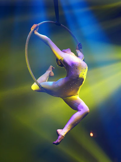 Circus acrobat performing on aerial hoop under colorful stage lights.