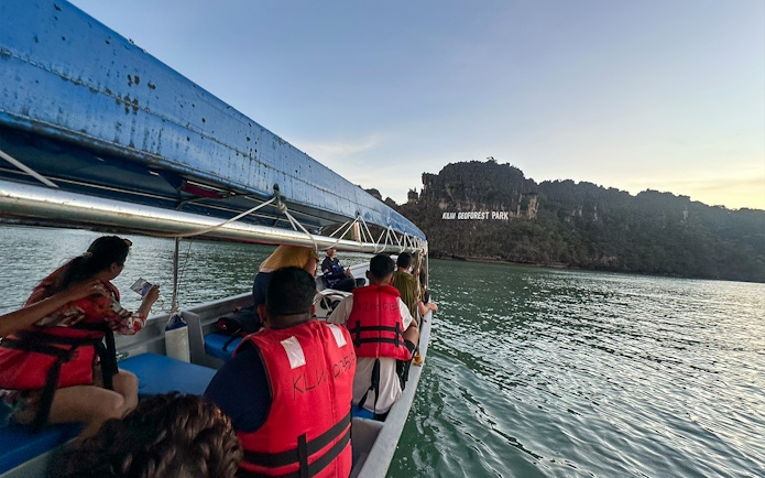 Tourists on a boat view Kilim Geoforest Park sign from the water in Langkawi.