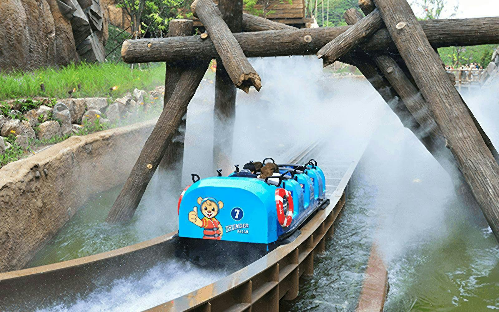 Water ride at summer festival with blue log flume passing under wooden beams.