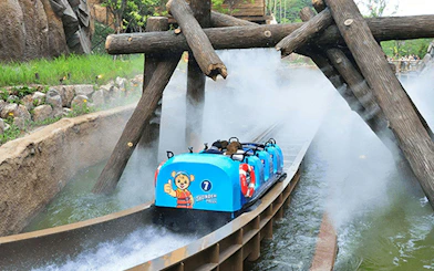 Water ride at summer festival with blue log flume passing under wooden beams.