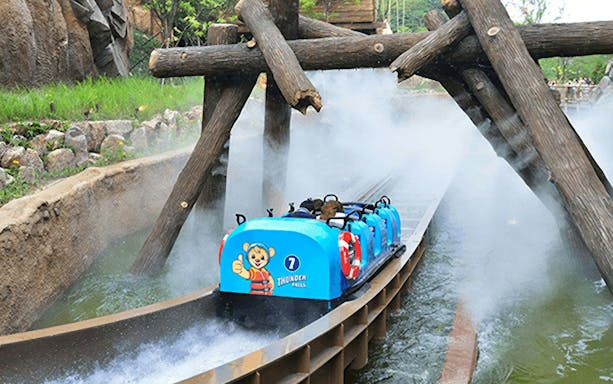 Water ride at summer festival with blue log flume passing under wooden beams.