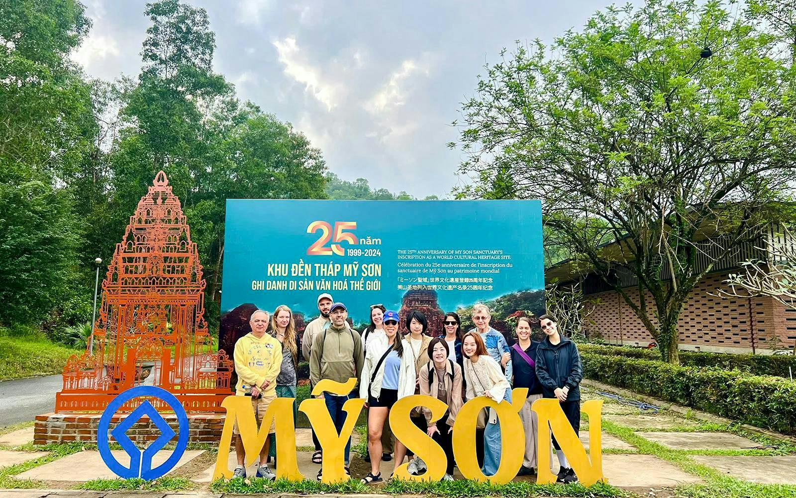 Group at My Son Sanctuary entrance, Vietnam, with temple replica and anniversary sign.
