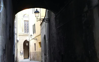 Narrow alleyway with historic buildings and lanterns in Pisa, part of the Romantic Walk exploration game.