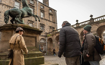 Tour group exploring a historical statue in Edinburgh courtyard.