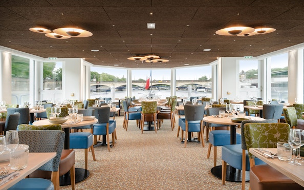 Seine River dinner cruise interior with tables set, Paris bridge view.
