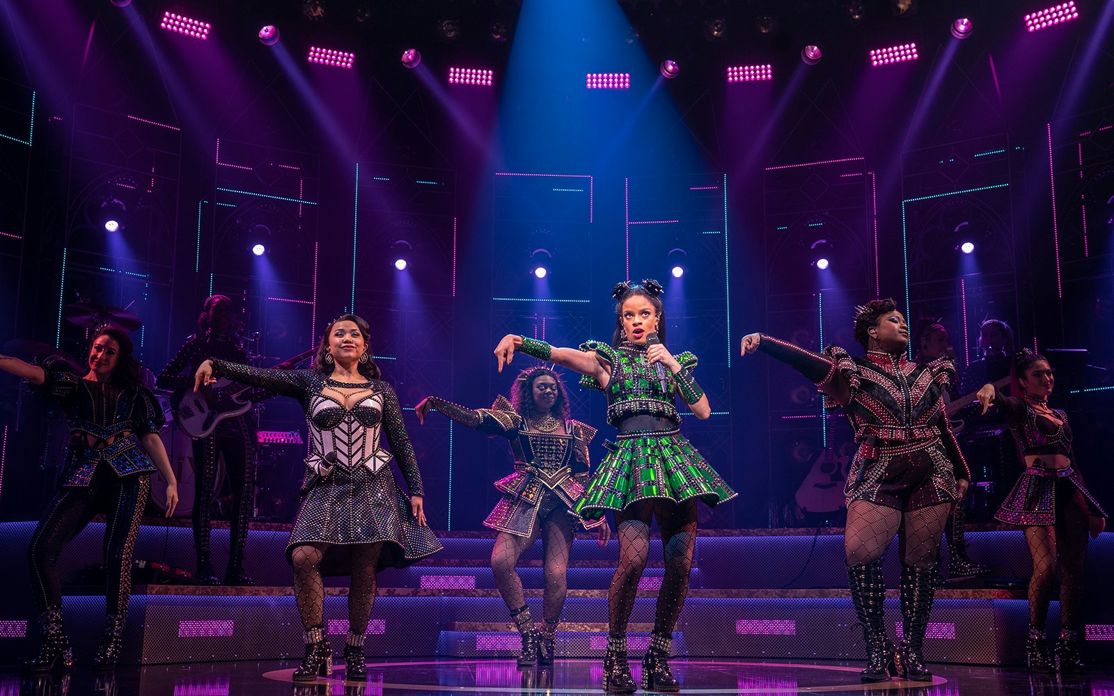Performers on stage during SIX: The Musical, vibrant costumes and dynamic lighting.
