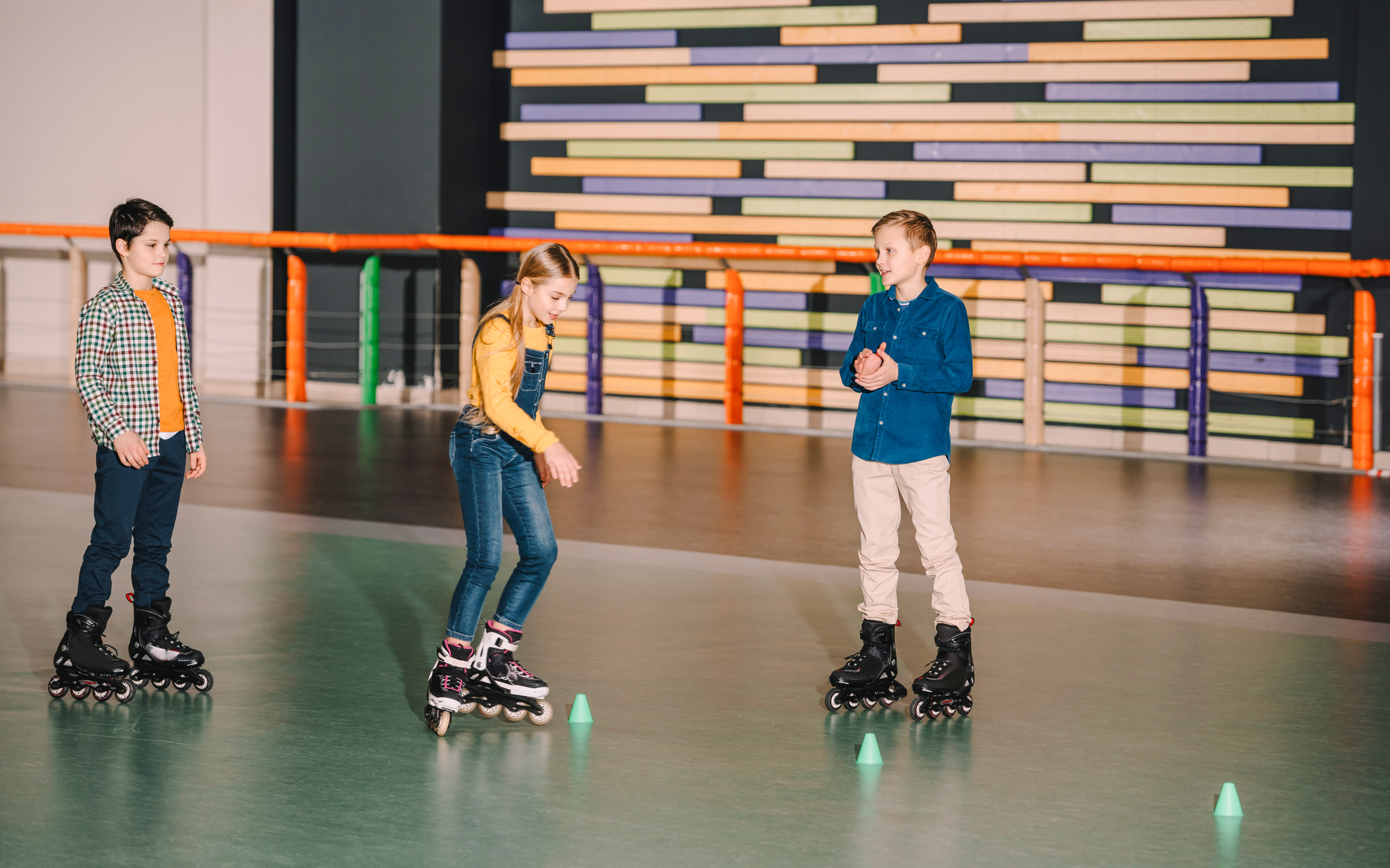 Roller skaters practicing on indoor rink with colorful wall background.