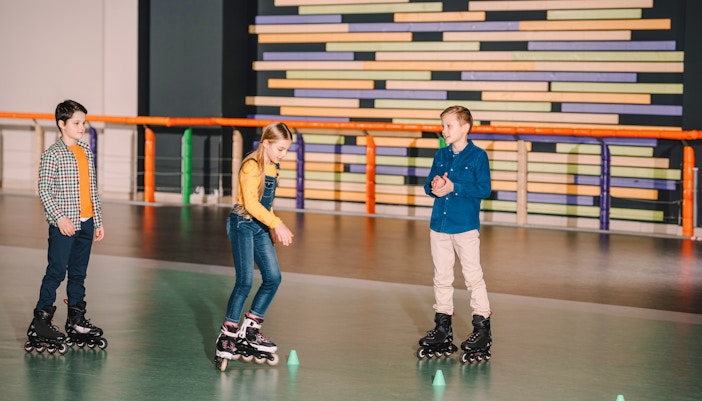 Roller skaters practicing on indoor rink with colorful wall background.