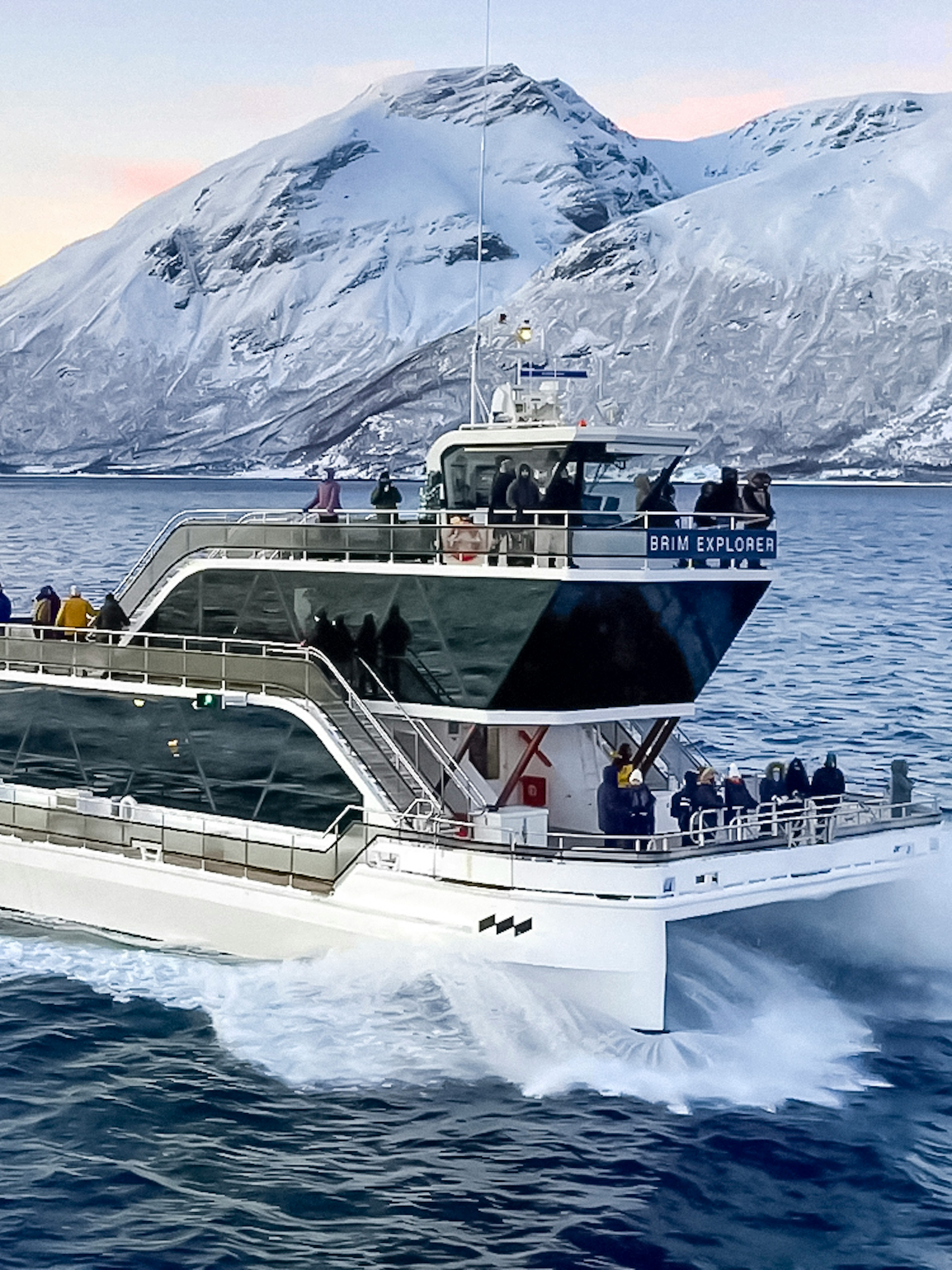Cruise ship on Arctic fjord near Tromso with snowy mountains in background.