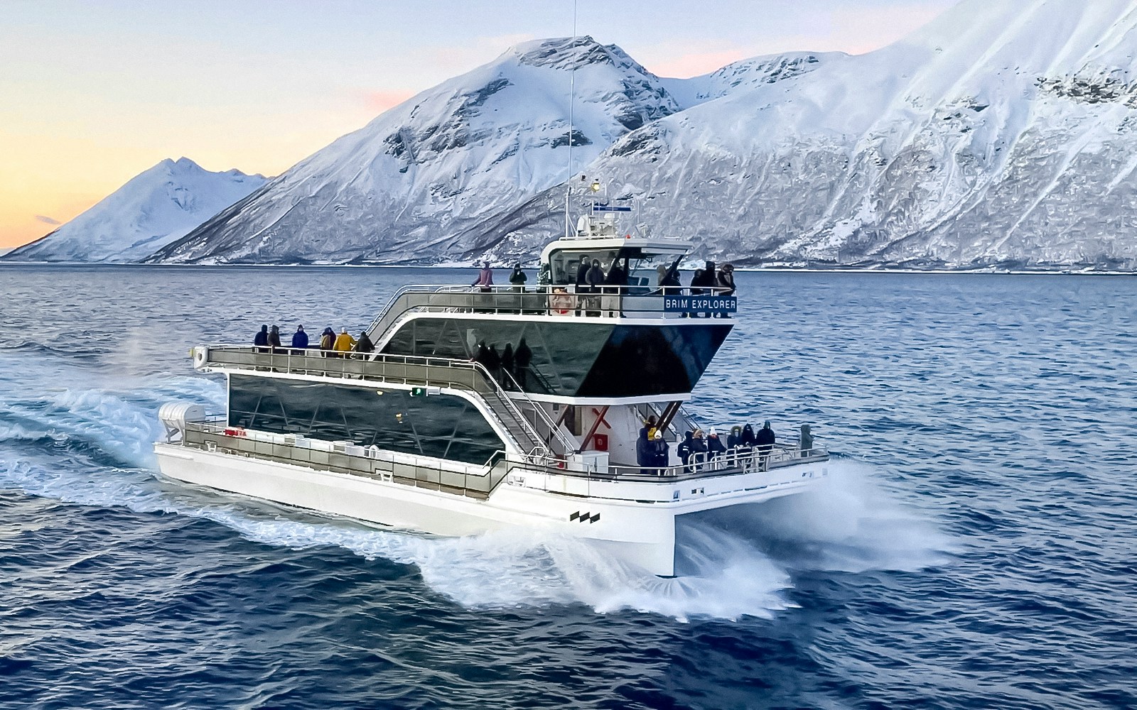 Cruise ship on Arctic fjord near Tromso with snowy mountains in background.