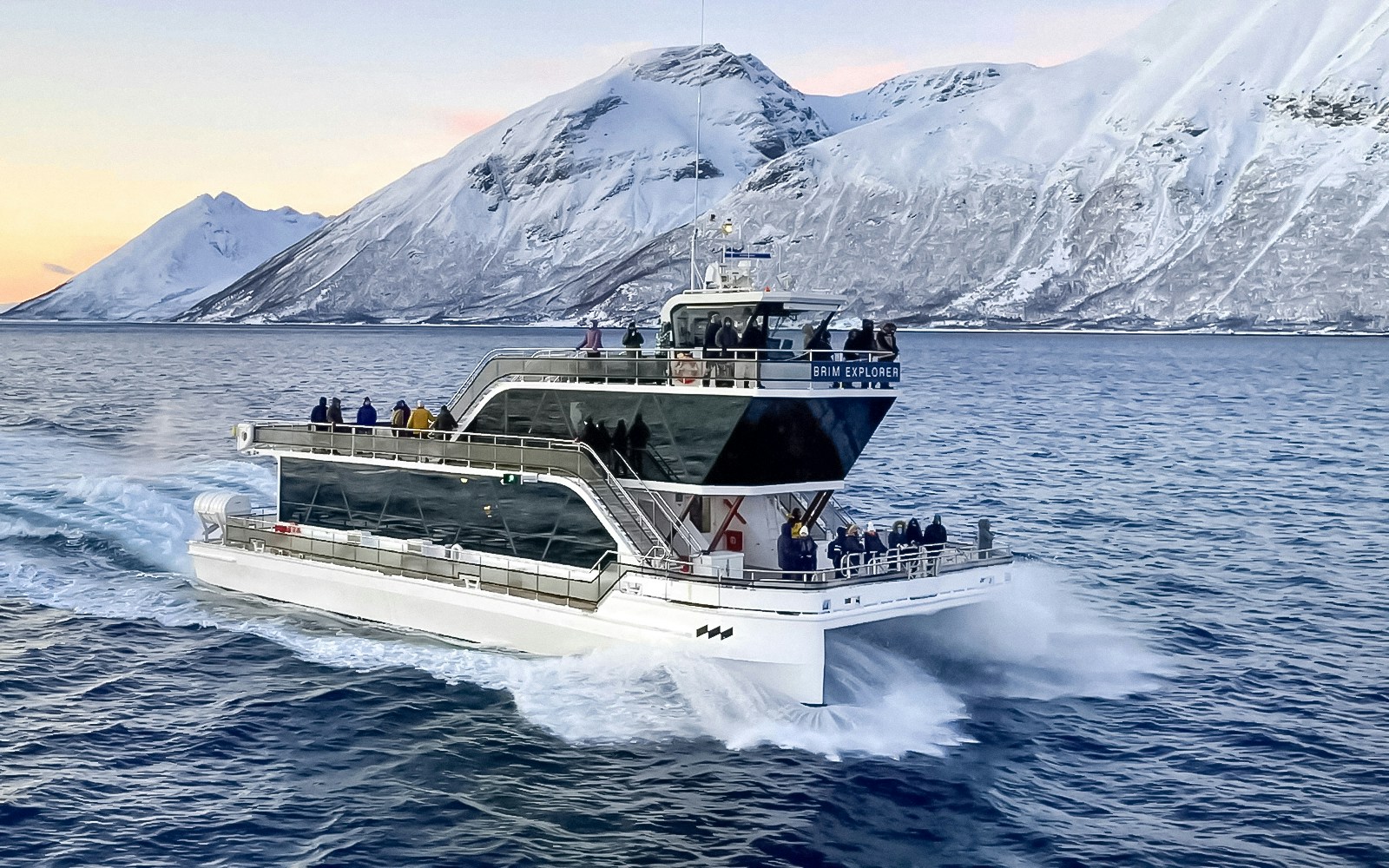 Cruise ship on Arctic fjord near Tromso with snowy mountains in background.