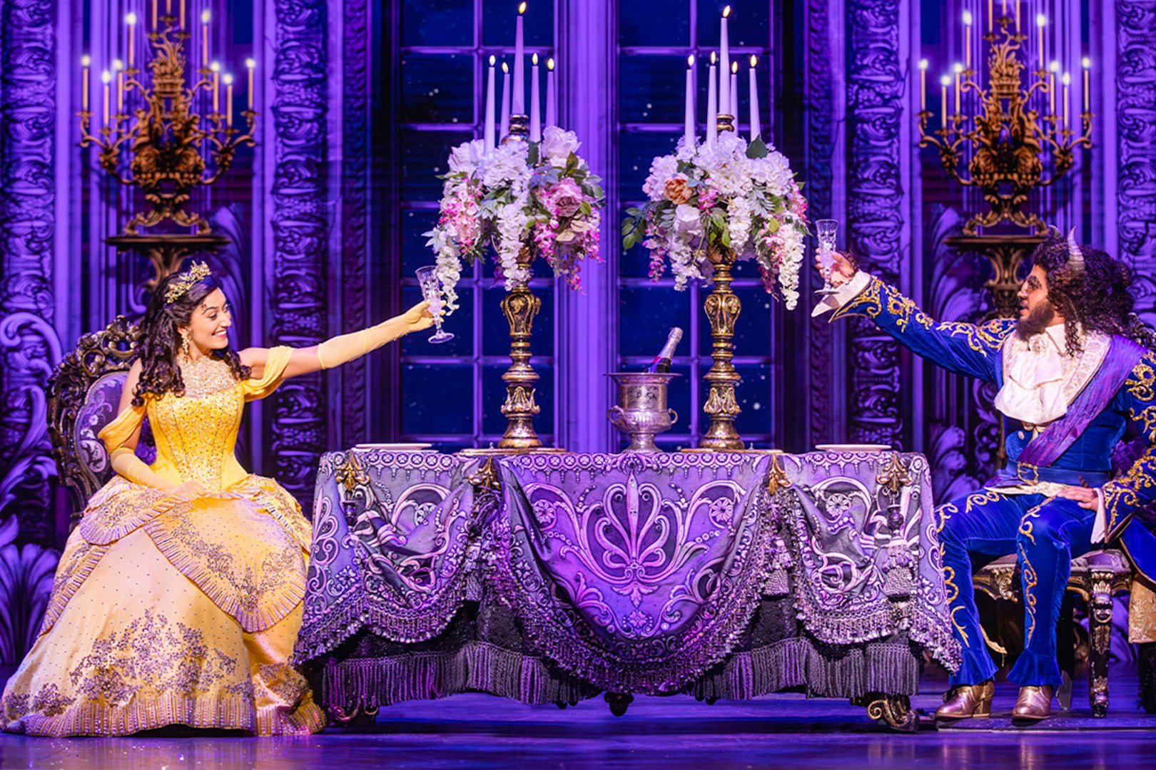 Belle and Beast toasting at an elegant table during a Beauty and the Beast performance.