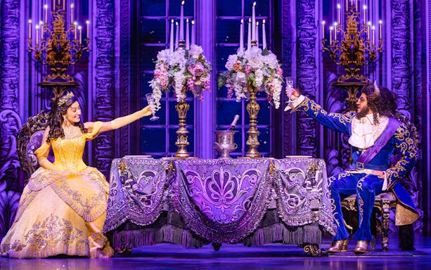 Belle and Beast toasting at an elegant table during a Beauty and the Beast performance.