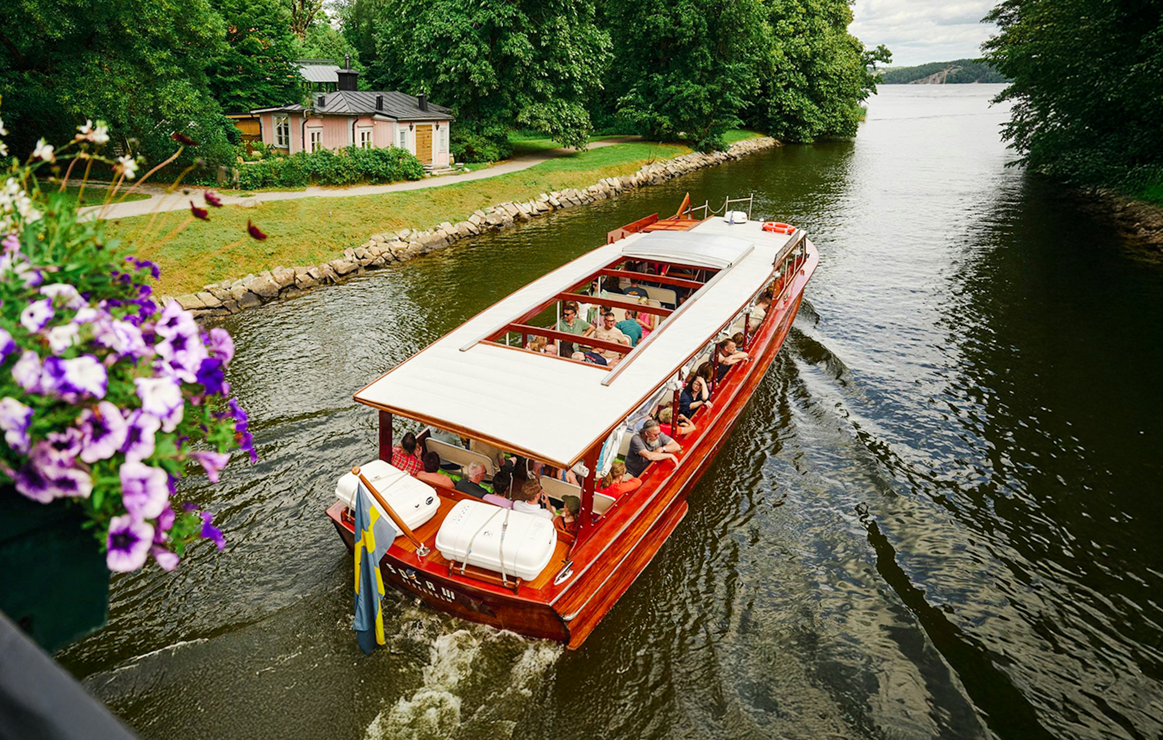 Classic wooden boat cruising through Stockholm Archipelago with passengers enjoying the view.