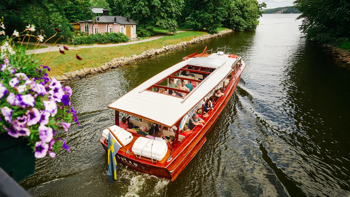 Classic wooden boat cruising through Stockholm Archipelago with passengers enjoying the view.
