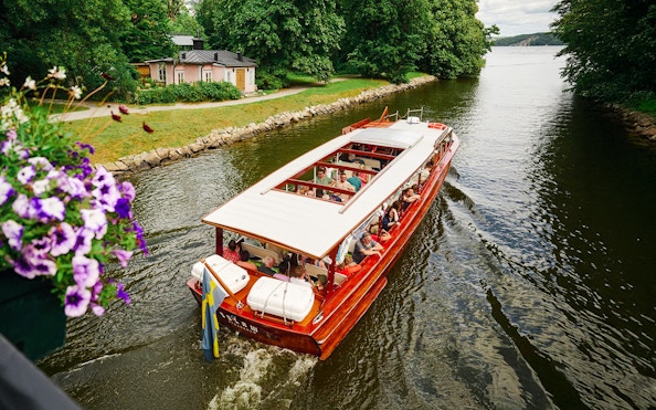 Classic wooden boat cruising through Stockholm Archipelago with passengers enjoying the view.