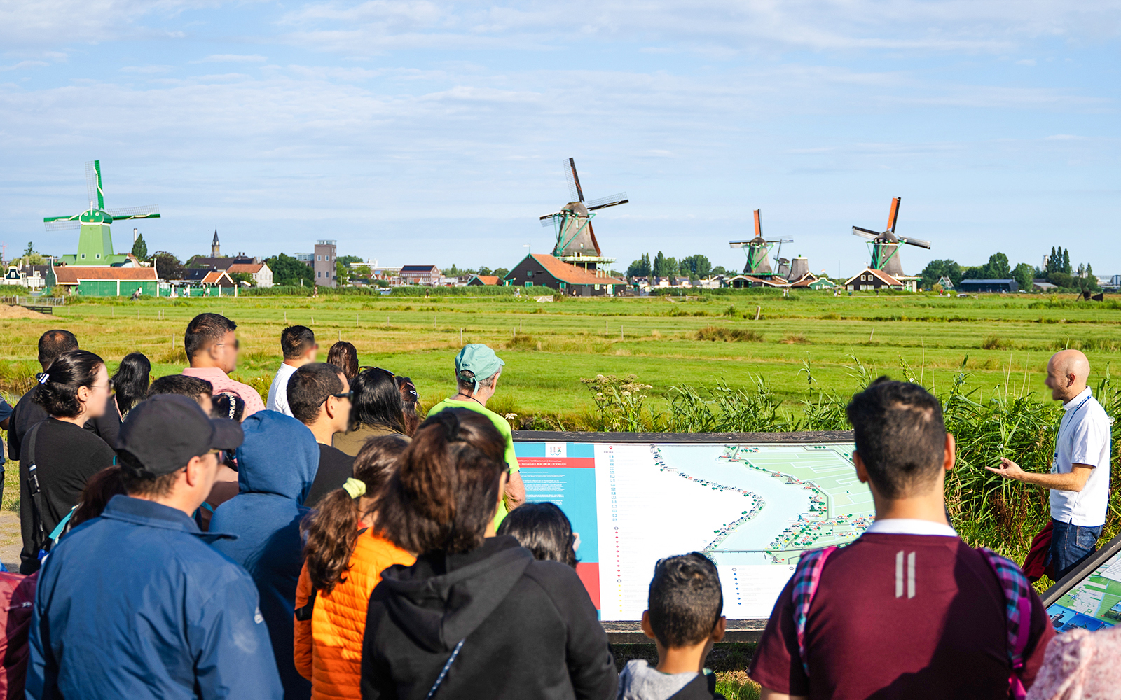 Tour group listening to a guide at Zaanse Schans with windmills in the background.