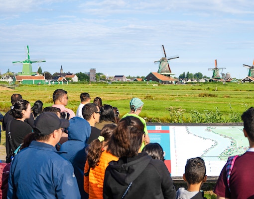 Tour group listening to a guide at Zaanse Schans with windmills in the background.