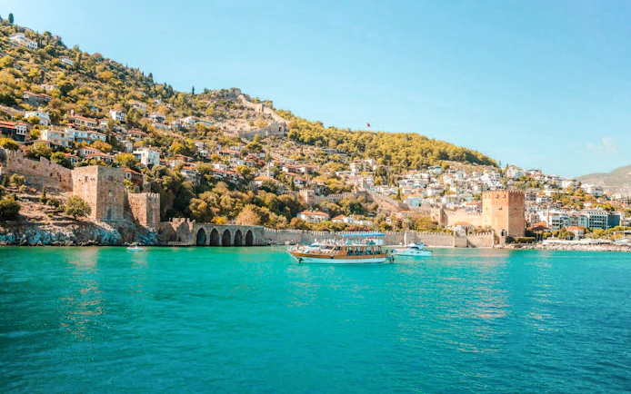 Boat on turquoise water near Alanya's historic Red Tower and hillside houses.