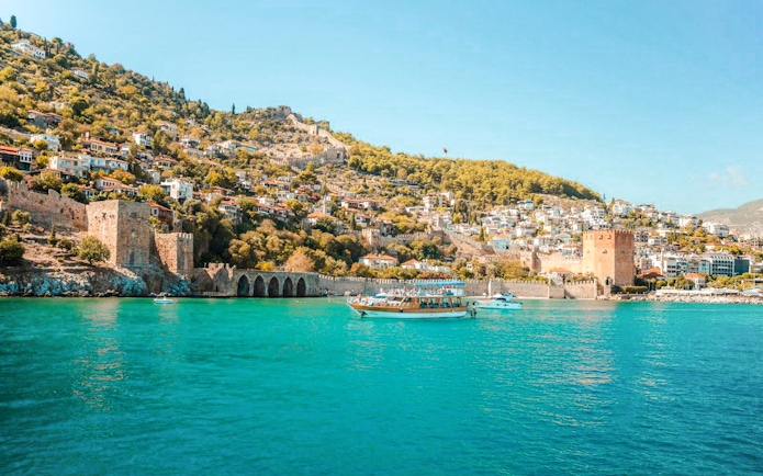 Boat on turquoise water near Alanya's historic Red Tower and hillside houses.