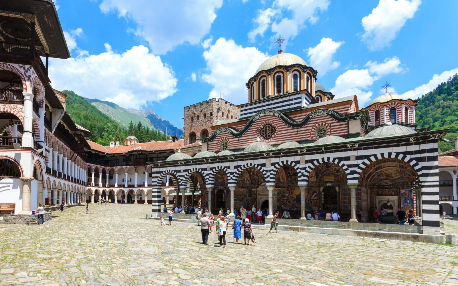 Rila Monastery Courtyard with striped arches and visitors in Bulgaria.