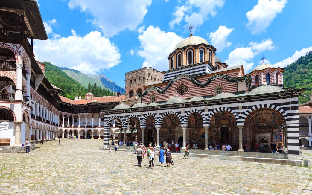 Rila Monastery Courtyard with striped arches and visitors in Bulgaria.