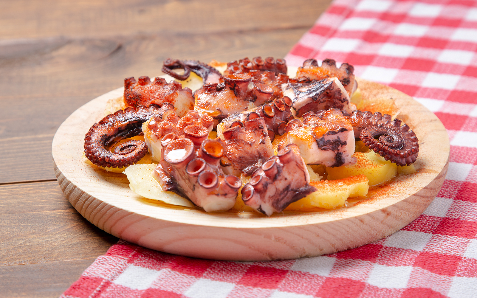 Pulpo a la gallega on wooden plate with potatoes and paprika.