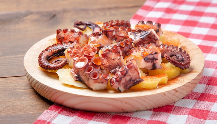 Pulpo a la gallega on wooden plate with potatoes and paprika.