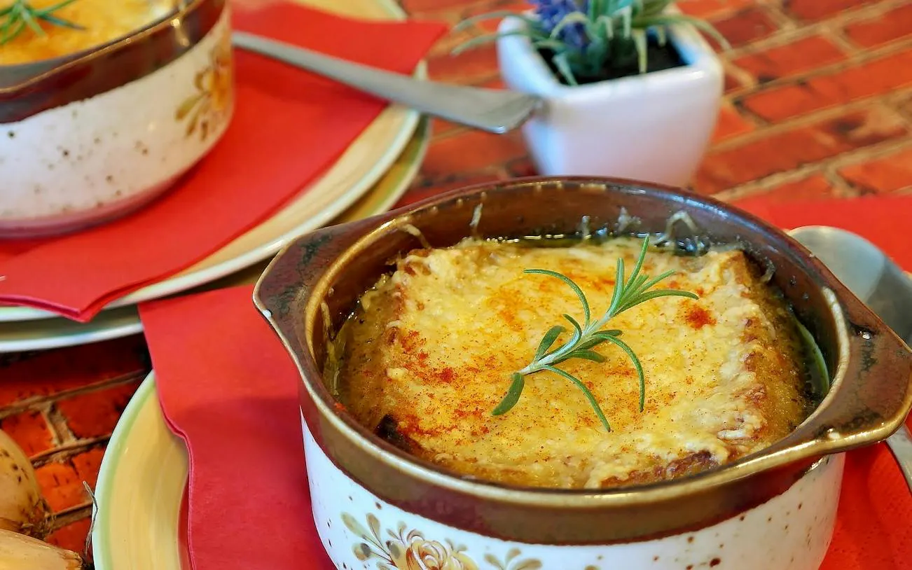 French onion soup served in a ceramic bowl with rosemary garnish, Montmartre food tour, Paris.