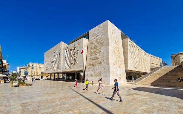 Parliament House in Valletta, Malta, with people walking nearby on a sunny day.