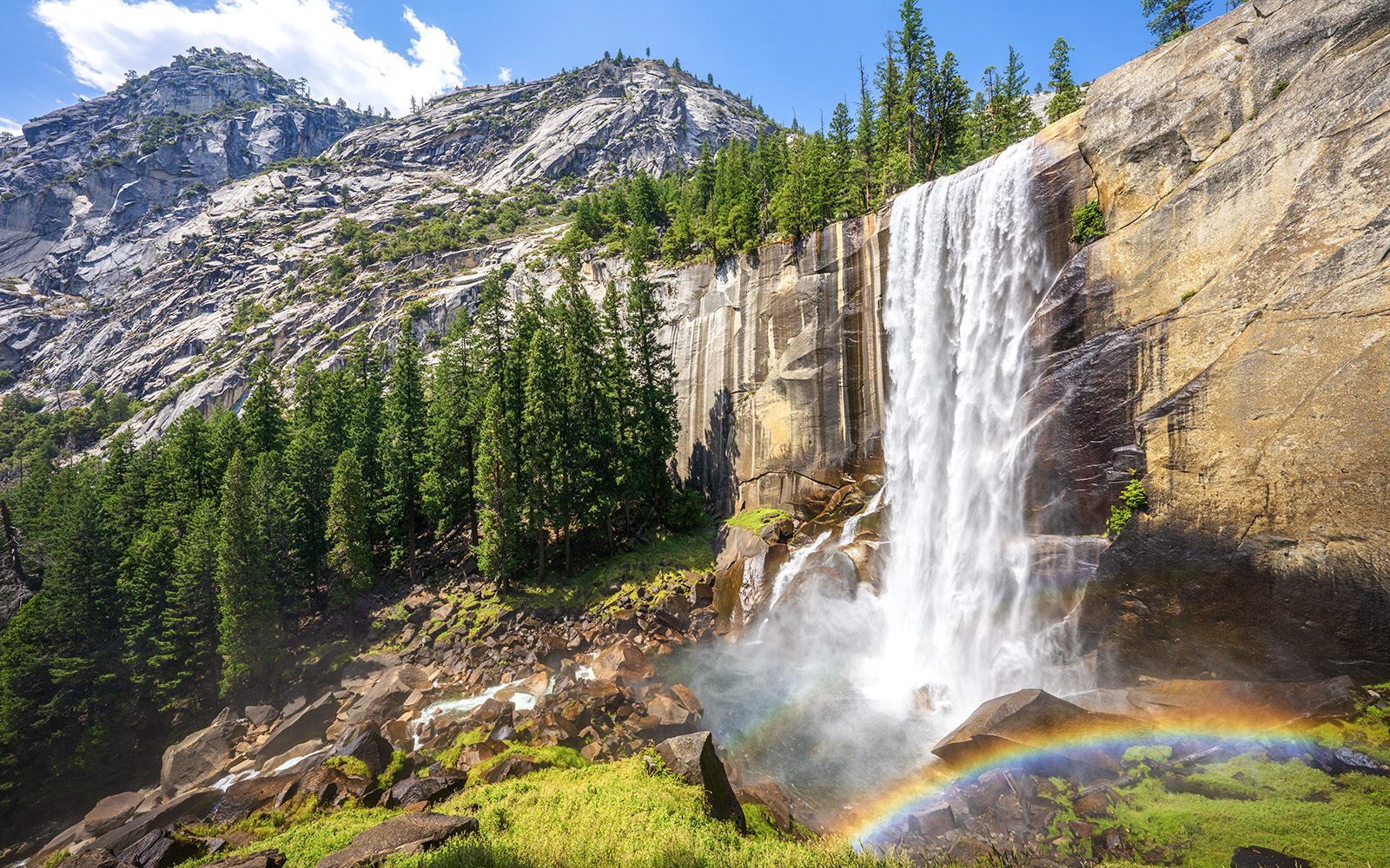 Waterfall cascading down rocks with rainbow at Mist Trail, Yosemite National Park.