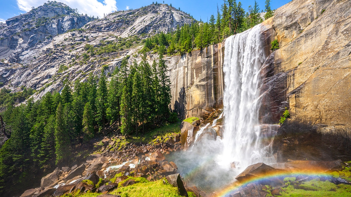 Waterfall cascading down rocks with rainbow at Mist Trail, Yosemite National Park.