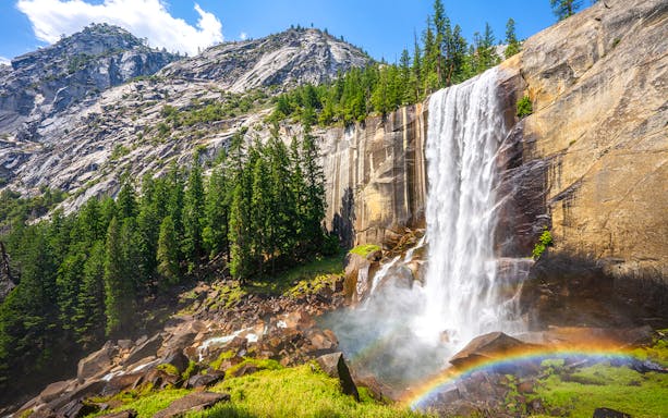 Waterfall cascading down rocks with rainbow at Mist Trail, Yosemite National Park.