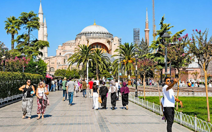 Visitors walking near Hagia Sophia in Istanbul, with minarets and gardens in view.