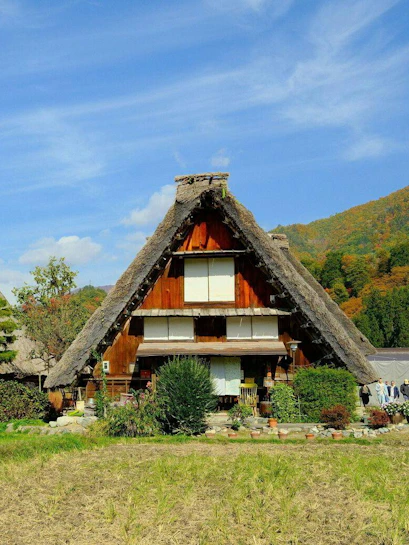 Thatch-roof farmhouse in Ogimachi, Shirakawa, Japan, with autumn foliage in the background.