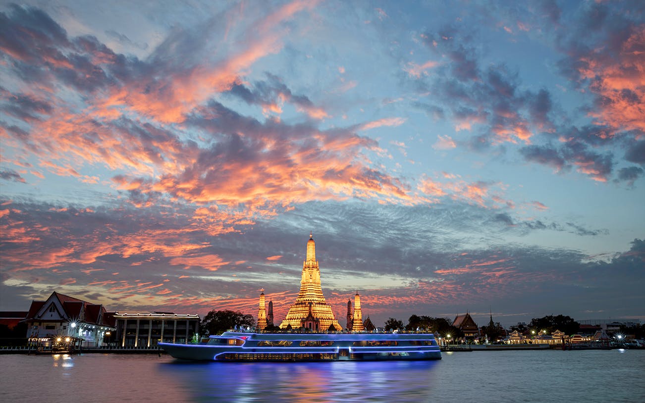 Cruise ship on Chao Phraya River with Wat Arun at dusk.