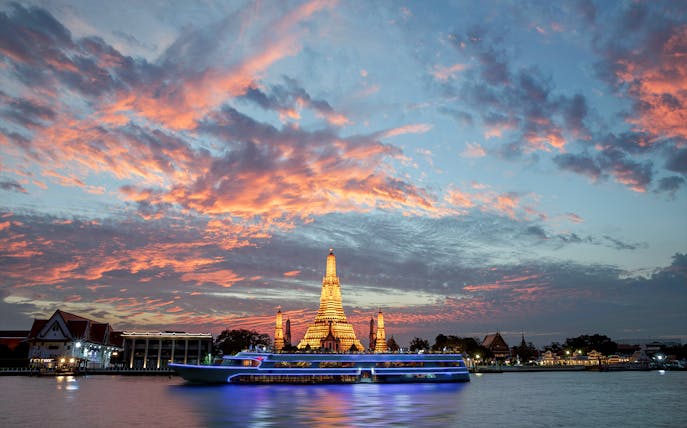 Cruise ship on Chao Phraya River with Wat Arun at dusk.