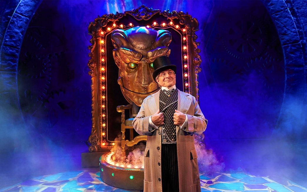 Stage scene from "Wicked" with a character in front of a large mechanical face.