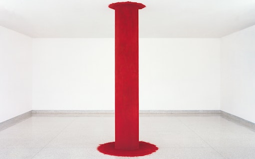 Red pillar installation by Anish Kapoor in a white gallery space.