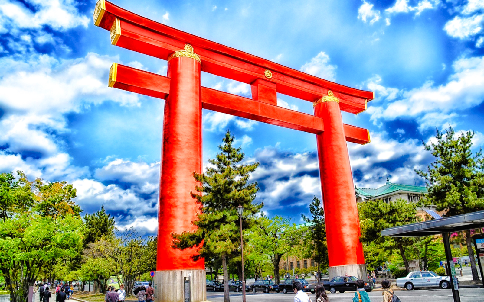 Large red torii gate at Fushimi Inari Taisha, Kyoto, with people and trees nearby.