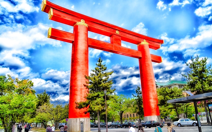 Large red torii gate at Fushimi Inari Taisha, Kyoto, with people and trees nearby.