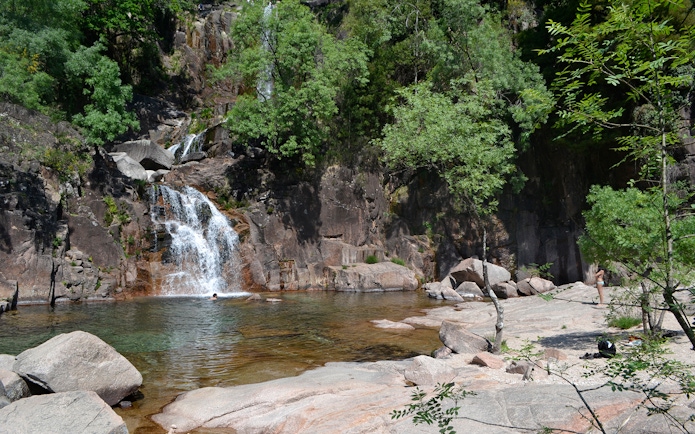 Waterfall and natural pool in Peneda Gerês National Park, Portugal, surrounded by lush greenery.